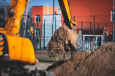 Sarı ağır kazıcı kumu kazıyor ve yol çalışmaları sırasında çalışıyor, yeni yolun inşaatı sırasında kumu boşaltıyor ve etrafta işçiler var.