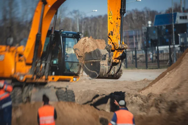 Yellow heavy excavator excavating sand and working during road works, unloading sand during construction of the new road with workers around