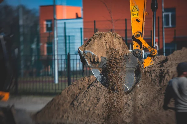 Yellow heavy excavator excavating sand and working during road works, unloading sand during construction of the new road with workers around