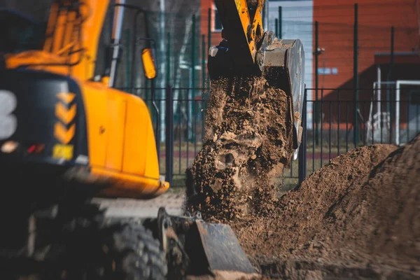 Yellow heavy excavator excavating sand and working during road works, unloading sand during construction of the new road with workers around