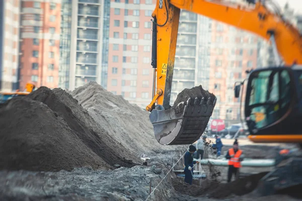 Yellow heavy excavator excavating sand and working during road works, unloading sand during construction of the new road with workers around