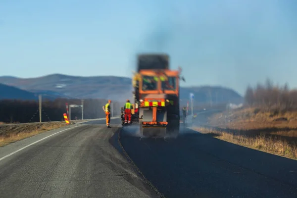 Asphalt paver machine and steam road roller during road construction and repairing works, process of asphalting and paving, workers working on the new road construction site, placing a laye