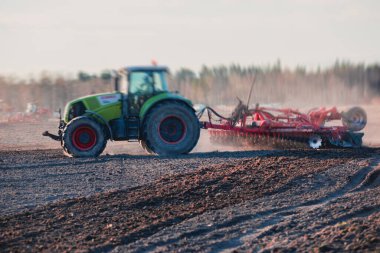 Disk harrow sistemine sahip bir traktör ekili tarım tarlasını, toprağı yıpratma ve hazırlama sürecini, gün batımında tarlada ekin ekme işini, tarım kavramını, Wor 'da harrow makinesini,