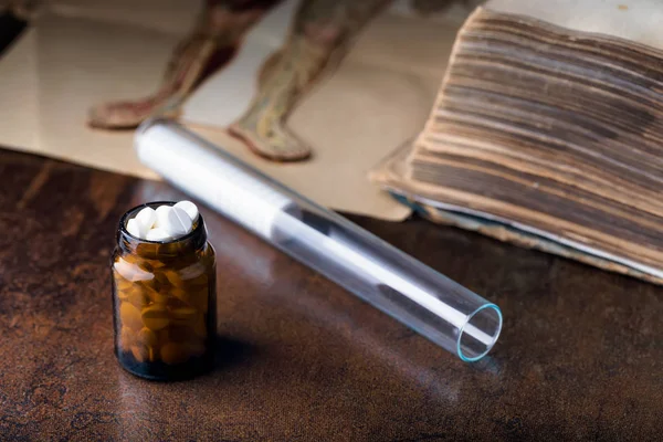 Banda białych tabletek ze szklanymi ampułkami i starą książką medyczną — Zdjęcie stockowe