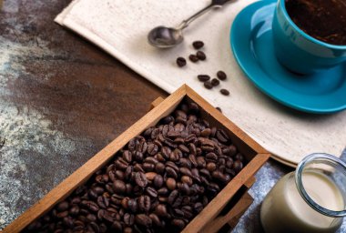 Bir fincan kahve ve içi kahve dolu ahşap kaplar.