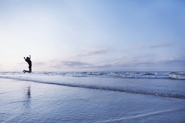 Женщина прыгает от радости на пляже на рассвете — стоковое фото