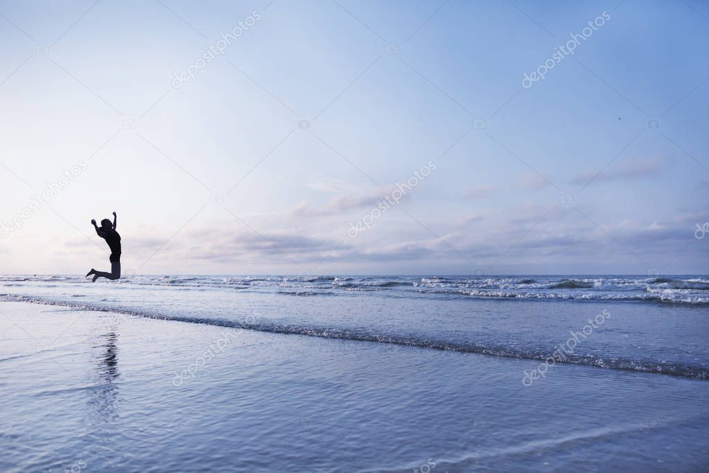 Woman jumping for joy on beach at sunrise