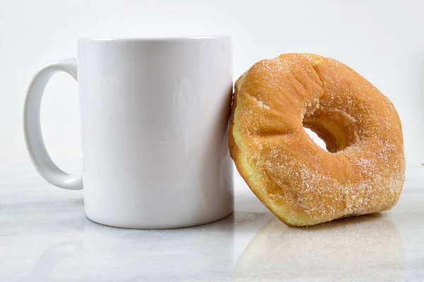 Donut de sucre frais reposant contre une tasse de café blanc — Photo