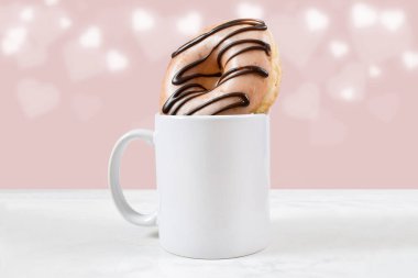 130 gramlık buzlu çikolatalı donutla dolu beyaz kahve kupası. Pembe arka planda Bokeh kalpleri parlıyor.