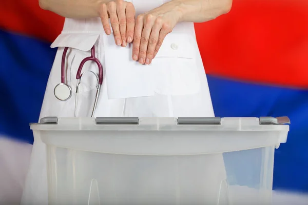 Doctor's hand casts ballot paper in the ballot box.