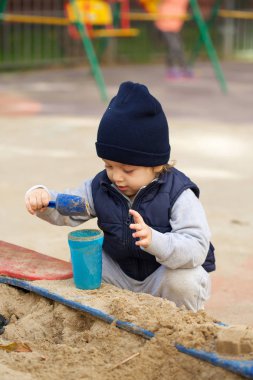 İki yaşında bir çocuk kum havuzunda oynuyor. Portre