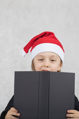 Noel Baba'nın şapka ve siyah klasik ceket dört yaşında çocuk. Noel Baba'nın şapka ve siyah kitap dört yıllık closeup oğlan masada oturur. Portre