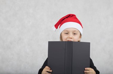 Noel Baba'nın şapka ve siyah klasik ceket dört yaşında çocuk. Noel Baba'nın şapka ve siyah kitap dört yıllık closeup oğlan masada oturur. Portre