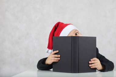 Noel Baba'nın şapka ve siyah klasik ceket dört yaşında çocuk. Noel Baba'nın şapka ve siyah kitap dört yıllık closeup oğlan masada oturur. Portre