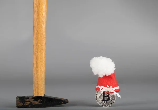 Bitcoin in a Santa Claus hat and a hammer on a gray surface. — Stock Photo, Image