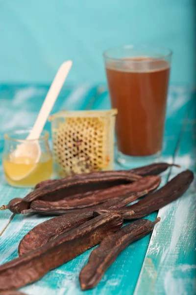 Carob pods and powder on a wooden surface. — Stock Photo, Image