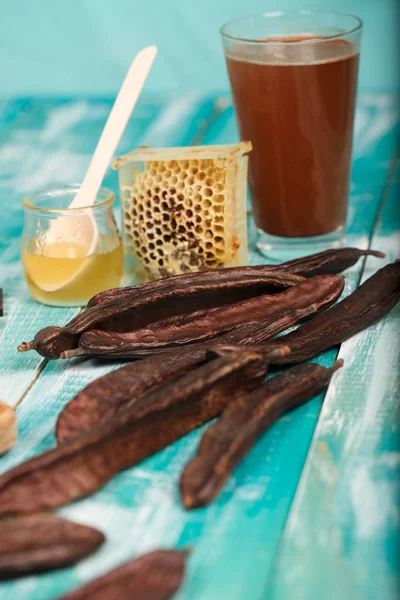 Carob pods and powder on a wooden surface. — Stock Photo, Image