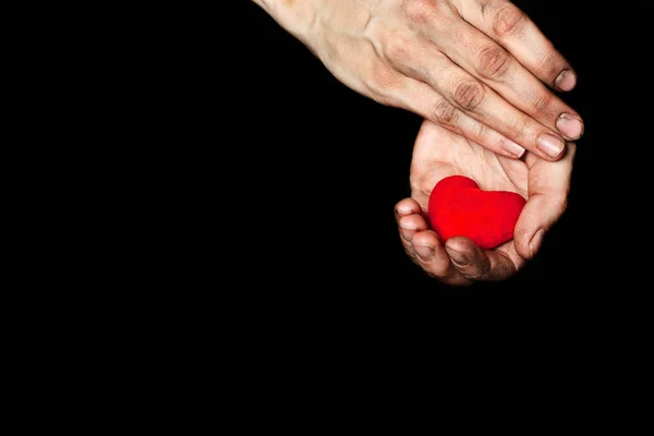 Palma de una campesina con un corazón rojo de felpa sobre un tejido negro . — Foto de Stock