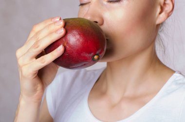 Genç beyaz Bayan mango meyve yüzüne yakın tutuyor. Portre
