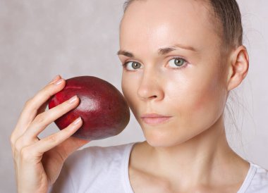 Genç beyaz Bayan mango meyve yüzüne yakın tutuyor. Portre