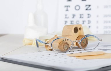 Eyeglasses for children on a eye chart close to eye pads.  clipart