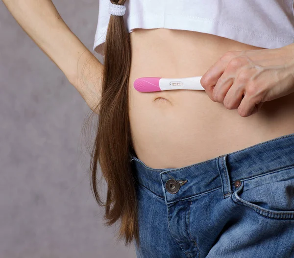 30岁至40岁的年轻女士穿着牛仔裤保持怀孕测试接近腹部 — 图库照片