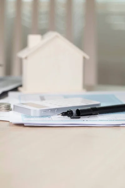 Black pen on papers. Calculator and small house in the backgroun — Stock Photo, Image