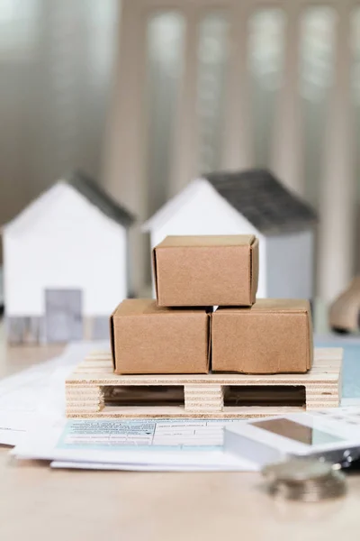 Palet con cajas de cartón frente a pequeñas casas de papel . — Foto de Stock