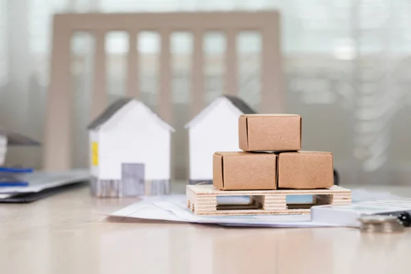 Palet con cajas de cartón frente a pequeñas casas de papel . — Foto de Stock