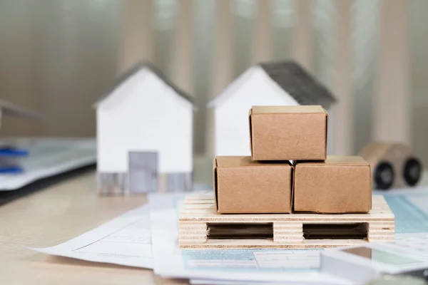 Palet con cajas de cartón frente a pequeñas casas de papel . — Foto de Stock