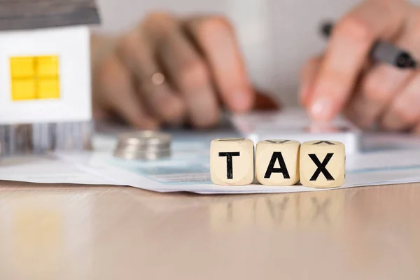 Palavra TAX composto de letras de madeira. Mão feminina com caneta em t — Fotografia de Stock