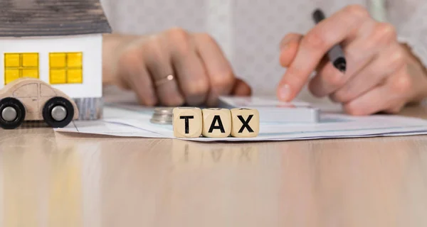 Palavra TAX composto de letras de madeira. Mão feminina com caneta em t — Fotografia de Stock