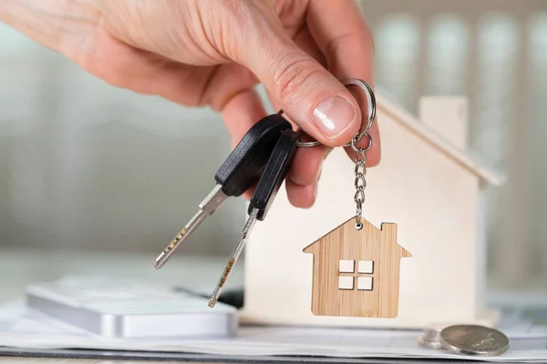 De huissleutel vrouwelijke houdt op een sleutel hanger voor een houten woning — Stockfoto