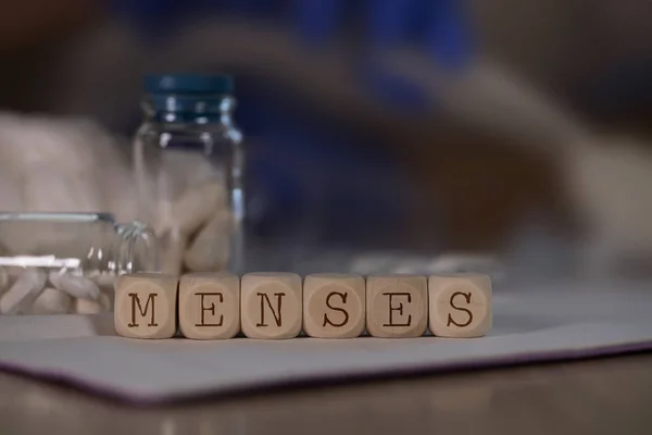 Слово MENSES состоит из деревянных кубиков. Таблетки, документы и ручка — стоковое фото