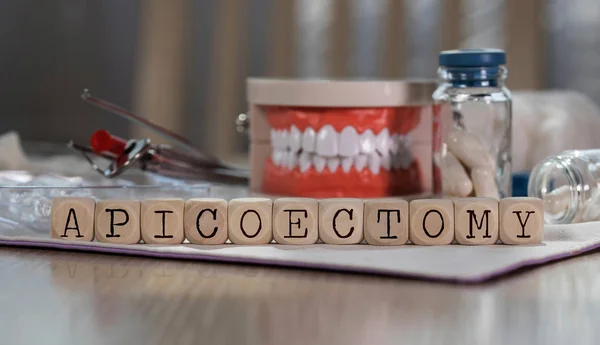 Slovo apikoektomie složené z dřevěných kostek. Prášky, dokumenty, pero Stock Obrázky