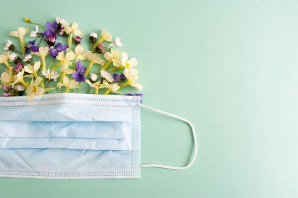 Mavi arka planda bitkisel çiçekleri olan koruyucu tıbbi maske. Yazı için yeri olan beyaz. Bahar alerjisi.