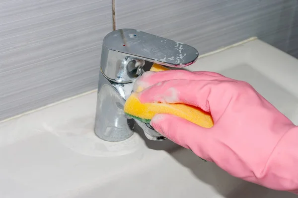 Banyoyu temizliyorum. Koruyucu eldivendeki bir el kirli musluğu sünger ve deterjanla yıkar. Kapat..