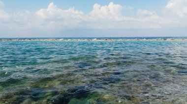 Mavi denizin kayalık kıyıları, dalgalar, gökyüzündeki beyaz bulutlar.