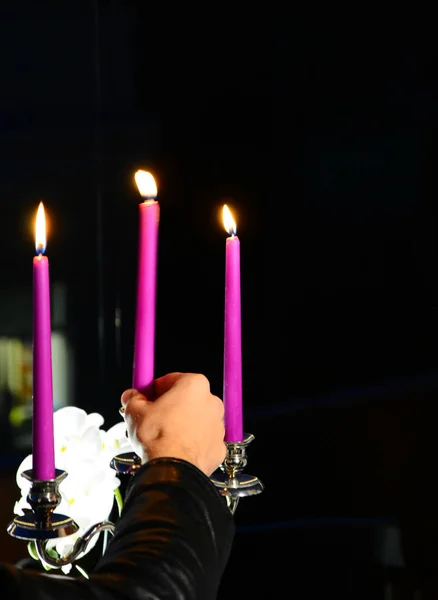 Lilac candles and a hand putting a new candle on a dark background