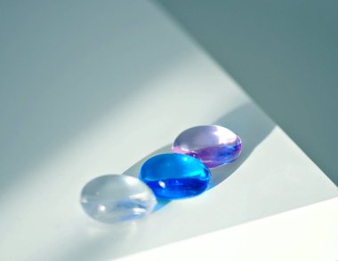 Beyaz, mavi ve eflatun renkli dekoratif şeffaf taşlar beyaz ve gri arka plan, yakın plan