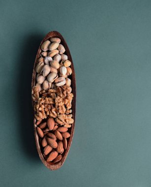 Badem, şam fıstığı, ahşap bir kasede ceviz koyu yeşil arka planda, yakın plan, boşluğu kopyala