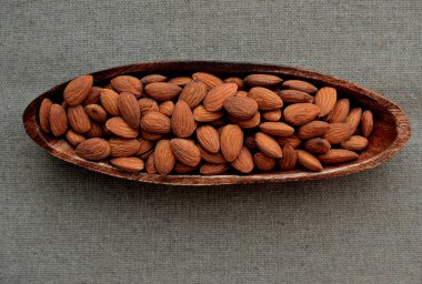 Bademler ahşap bir kasede, peçete arka planında, en üstte.