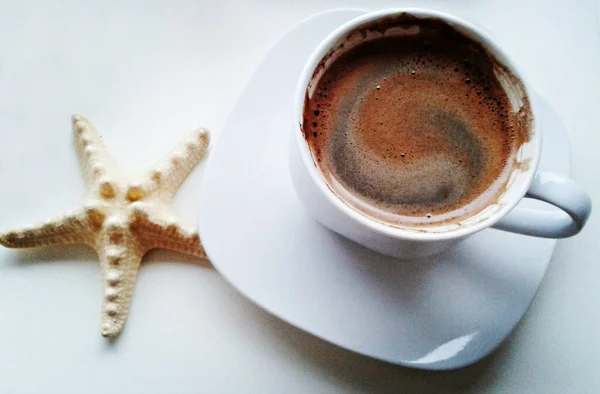 white cup of coffee on white background and starfish, close-up