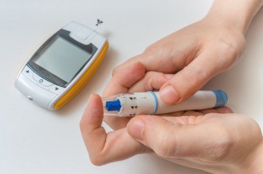 Diabetes concept. Hands holds needle for measuring glucose level with glucometer. clipart