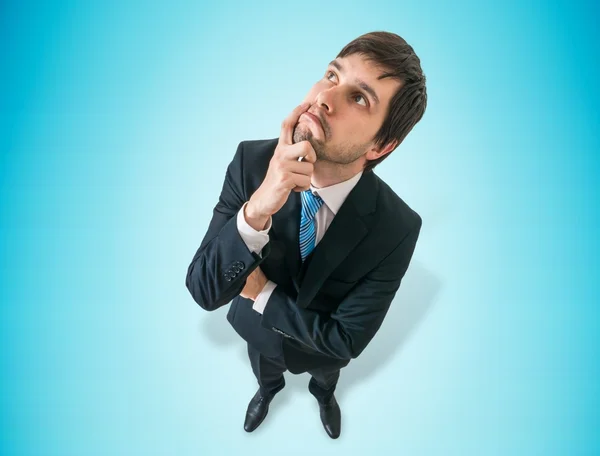 Young thoughtful businessman is thinking on blue background. — Stock Photo, Image