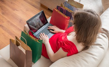 Genç kadın evde kanepede oturan ve laptop ile online alışveriş.