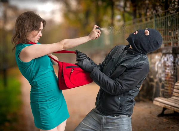 Self defense concept. Young woman was attacked by man in balaclava and is using pepper spray. — Stock Photo, Image