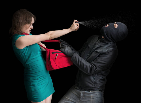 Self defense concept. Young couple is defending with pepper spray against thief in balaclava. Low key photo.