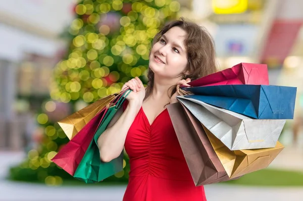 Молодая женщина делает подарки на Рождество в магазине и несет много мешков . — стоковое фото