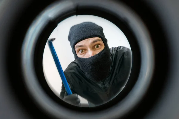 Vista através do poço. Ladrão ou ladrão mascarado com balaclava está segurando pé de cabra atrás da porta . — Fotografia de Stock